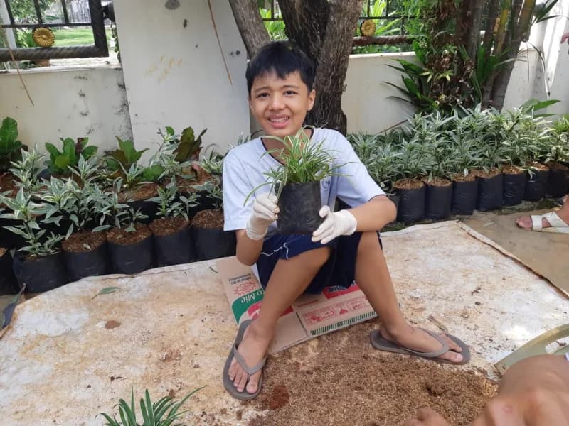 Seorang siswa tersenyum menunjukkan tanaman hias dalam polybag hasil tanamnya