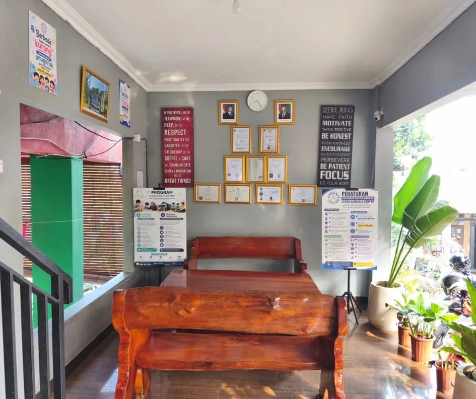 Ruang tamu Karunia Center dengan deretan sertifikat lembaga, papan program, dan papan peraturan kunjungan di dinding