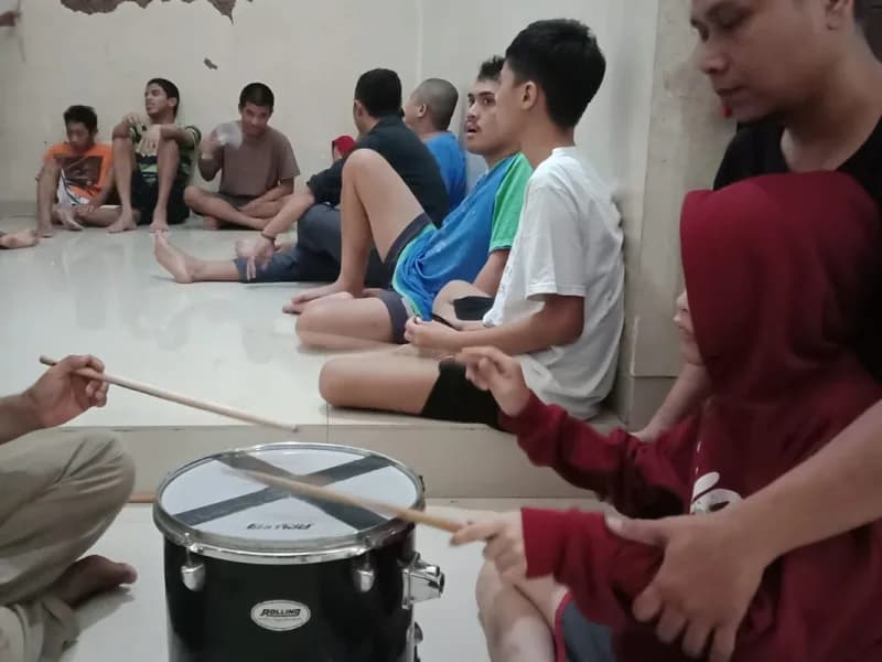 Seorang siswa menirukan pukulan snare drum pendamping, siswa lain menyimak dari tepi ruangan