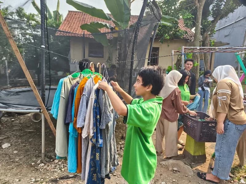 Seorang siswa menggantung pakaian pada hanger di tali jemuran halaman belakang