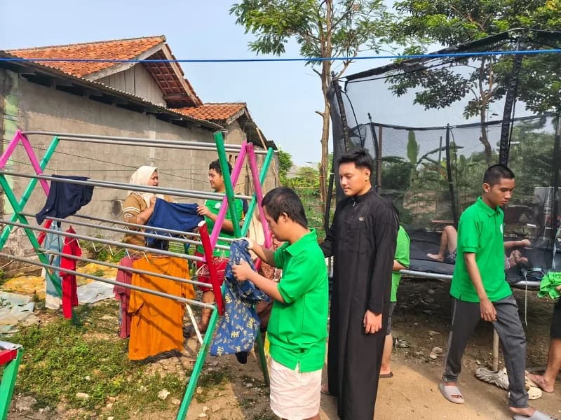 Siswa merapikan pakaian di rak jemuran bersama pendamping di halaman belakang
