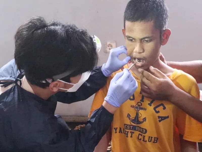Petugas kesehatan bermasker dan bersarung tangan memeriksa gigi seorang siswa